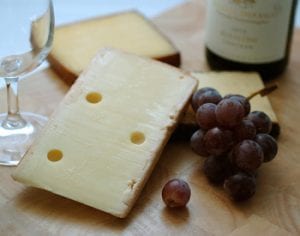 sliced cheese grapes wine on wood cutting board